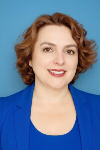 Professional headshot of Ana Olmedo, founder of Bravaura Consulting, wearing a blue blazer and smiling confidently
